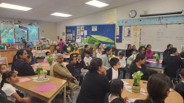 Classroom filled with students and family members sitting in chairs listening to a presentation.